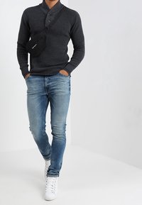 Ciemnoszary sweter z prążkowanej tkaniny z kołnierzykiem henley, sparowany z jasnoniebieskimi dżinsami i białymi trampkami typu high-top. Akcent w postaci czarnej torebki na ramię.