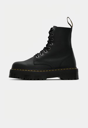 Botas de tobillo de cuero negro con cordones, suela de goma texturizada gruesa y detalle de costura amarilla alrededor de la plataforma.