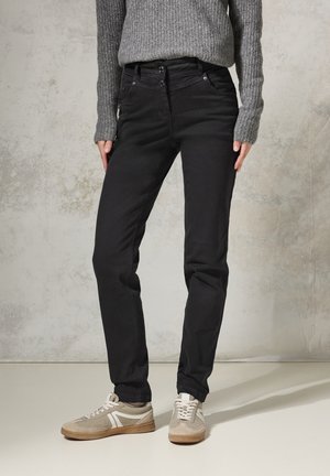 Zwarte, slim-fit jeans met een gladde textuur en vijf zakken, gecombineerd met grijze sneakers met witte accenten en lichtbeige zolen.