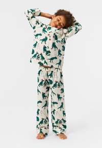 Pidžama set s krem pozadinom i uzorcima zelenih dinosaura i blagdanskim motivima. Košulja s gumbima, hlače s elastičnom gumom.