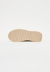 Suola di una scarpa in gomma beige chiaro, caratterizzata da una texture profondamente rigata per garantire trazione. Bordo liscio senza loghi o marcature visibili.