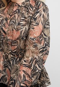 Blouse transparente arborant un imprimé floral et feuillage multicolore dans des tons de rose, noir et olive. Taille élastiquée avec manches bouffantes.