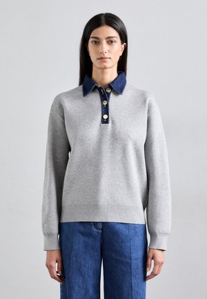 Pull en tricot gris avec un col en denim, des boutons dorés et des poignets côtelés. Porté avec un jean bleu à jambes larges, mettant en valeur une coupe décontractée.