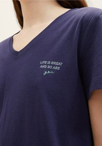 Marinblå v-ringad t-shirt i mjukt tyg, med vit och grön broderad text: "LIVET ÄR STORT OCH SÅ ÄR DU" på framsidan.