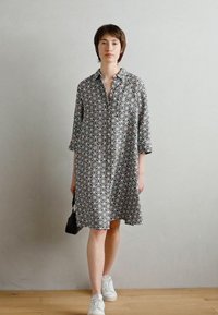 Abito a fantasia bianco e nero con collo alla francese, maniche a tre quarti e una vestibilità ampia, abbinato a sneakers bianche.