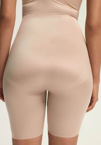Beżowe szorty modelujące z dopasowanym krojem, teksturowanym materiałem i długością do połowy uda, z subtelnymi detalami wzoru.