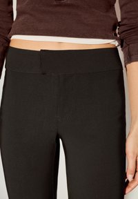 Crne helanke s visokim elastičnim pojasom, s glatkom teksturom i suptilnim šavovima, prikazane od struka naniže.