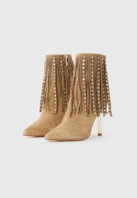 Tan suède enkellaarzen met spitse neuzen, gouden hoge hakken, franje versierd met gouden studs langs de schacht.