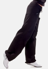 Black sweatpants with a relaxed fit, featuring elasticized cuffs, side pockets, and a smooth texture. Paired with white athletic shoes.