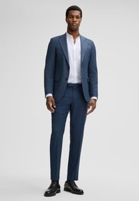 Männlicher blauer Anzug, maßgeschneideter Schnitt, strukturierter Stoff, einreihige Jacke, Reverskragen, slim-fit Hose, kombiniert mit einem weißen Hemd und schwarzen Schuhen.