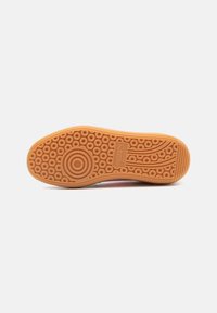 Suela de sneaker de goma con un diseño estampado que presenta recortes circulares y ranuras. Color: marrón claro con un acabado texturizado.