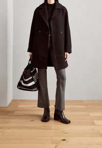 Cappotto nero con dettagli di cuciture bianche, top nero, pantaloni grigi a fantasia e stivali neri con tacco. Presenta anche una borsa a righe.