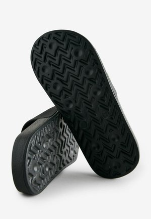 Juodos gumos šlepetės su tekstūruota išorine dalimi, turinčia zigzago raštą ir apvaliais dėklais, užtikrinančiais geresnį sukibimą.