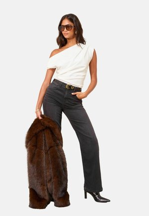White one-shoulder top, high-waisted black jeans, brown fur coat, and black heeled boots. Accessories include oversized sunglasses and a belt.