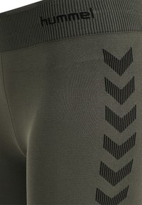 Olijfgroene legging met een geribde tailleband, versierd met zwarte chevronpatronen aan de zijkant, gemaakt van rekbare stof voor comfort.