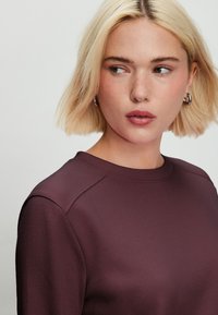 Bordó pulóver kerek nyakkivágással és finom textúrájú anyaggal. Raglánujjas dizájn, puha tapintású, látható mintázat nélkül.