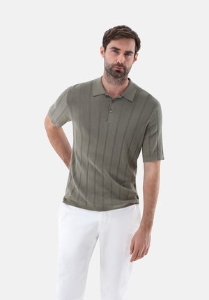 Khaki-grünes Poloshirt mit kurzen Ärmeln, strukturierten vertikalen Streifen und einer Drei-Knopf-Blende, getragen mit weißen Hosen.