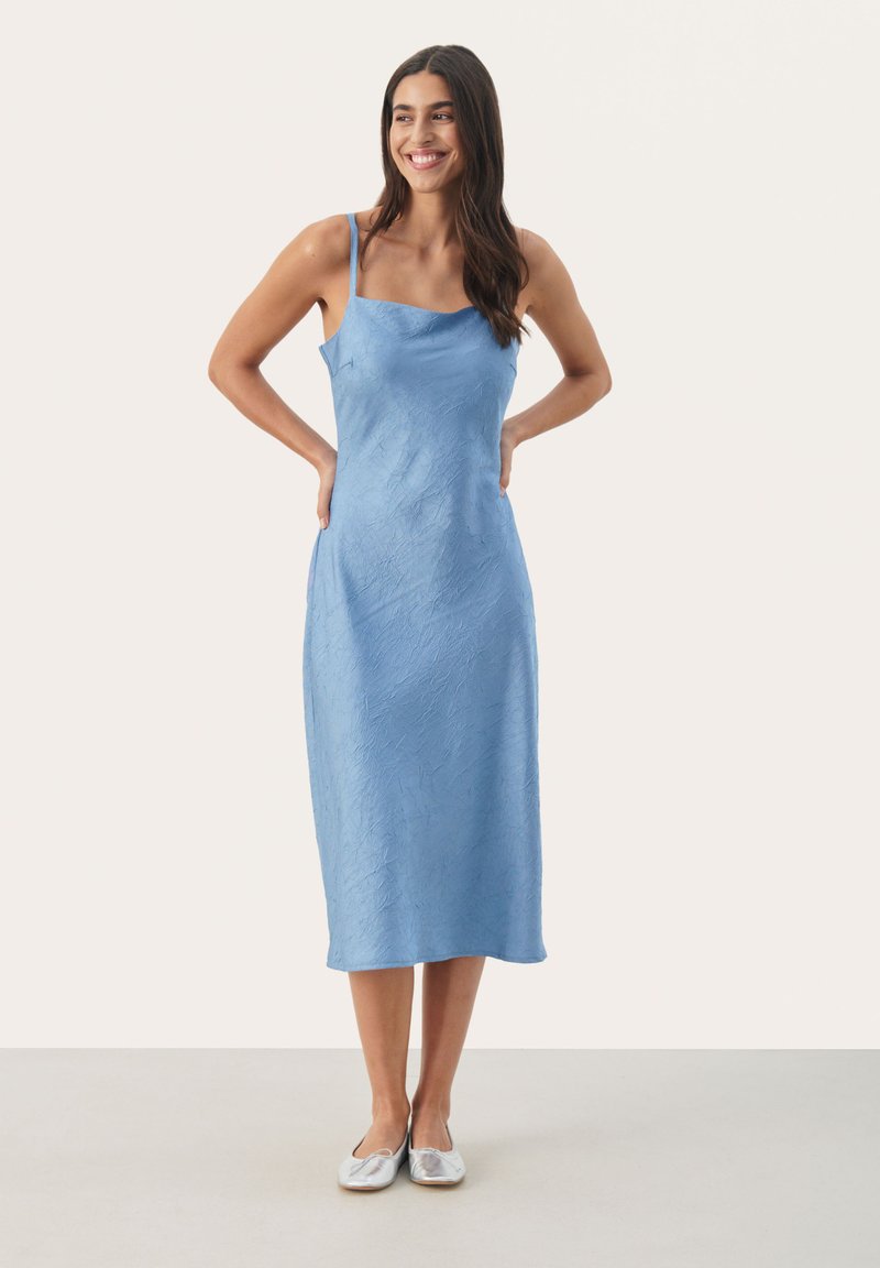 Rochie midi de culoare albastru deschis, cu bretele subțiri, țesătură texturată, decolteu pătrat și ușor în formă de A, asortată cu pantofi plata argintii.