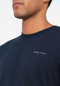 Μπλούζα φανέλα από βαμβάκι σε ναυτικό μπλε, με στρογγυλή λαιμόκοψη και κοντά μανίκια, με λογότυπο "TOMMY JEANS" κεντημένο στο στήθος. Μαλακή υφή.