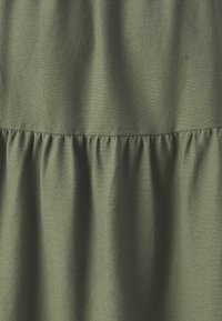 Una tela verde oliva con una textura suave presenta un detalle de recogido a lo largo de la costura, creando un sutil efecto de volantes.