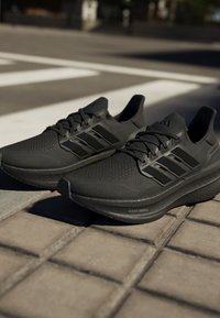Crne atletske tenisice s gornjim dijelom od teksturirane mrežice, s tri crne pruge i uloškom s oznakom "LIGHTBOOST." Uključene su ravne vezice.