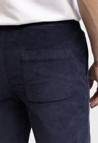 Pantalones de pana azul marino con una superficie texturizada, que cuentan con un bolsillo trasero. La cintura es elástica para mayor comodidad. Vista en primer plano desde el lado.