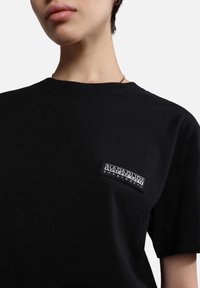 Svart bomull T-shirt med en sydd svart och vit logotyp på vänster bröst. Korta ärmar med en klassisk rund halsringning.