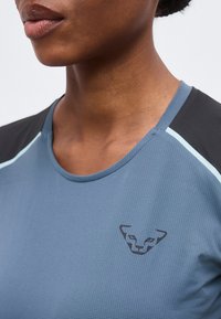 Κοντινό πλάνο ενός ατόμου που φοράει μπλε και μαύρο αθλητικό τοπ με διακριτικό λογότυπο προσώπου τσιτάχ στο στήθος.