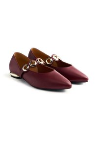 Chaussures plates bordeaux avec un bout pointu, présentant des accents circulaires dorés et un petit talon. Texture en cuir lisse et côtés ouverts.