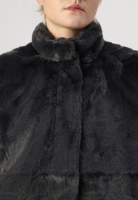 Black faux fur shawl with a high collar and soft texture. Features seamless stitching and a smooth finish.