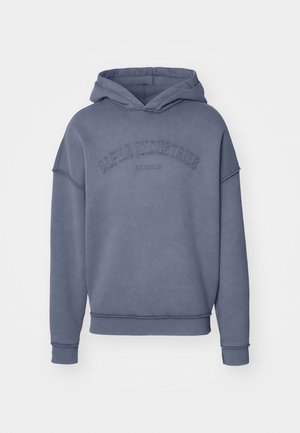 Hoodie w stonowanym niebieskim kolorze, wykonany z miękkiego materiału, z haftowanym logo "Alpha Industries" na piersi oraz ściągaczami przy rękawach i u dołu.