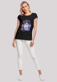 Svart kortermet t-skjorte med et fargerikt grafisk design av Askepott. Kombinert med hvite skinny jeans og hvite joggesko.
