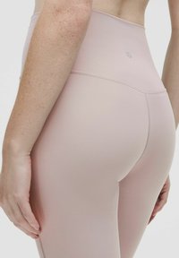 Svetloružové legíny s vysokým pásom vyrobené z hladkej, elastickej látky s plochými švami, s jemným logom na zadnej strane a priliehavým strihom.