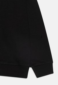 Schwarze Sweatshirtärmel mit einem gerippten Bündchen und glatter Textur, versehen mit einem kleinen Logodetail in der Nähe der Naht.