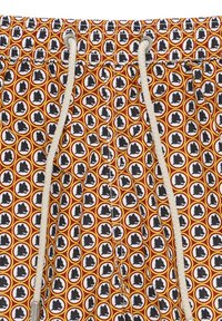 Shorts de bain avec un motif répétitif de silhouettes noires dans des cercles orange et blancs, dotés d'une taille à cordon de serrage et d'un tissu texturé.