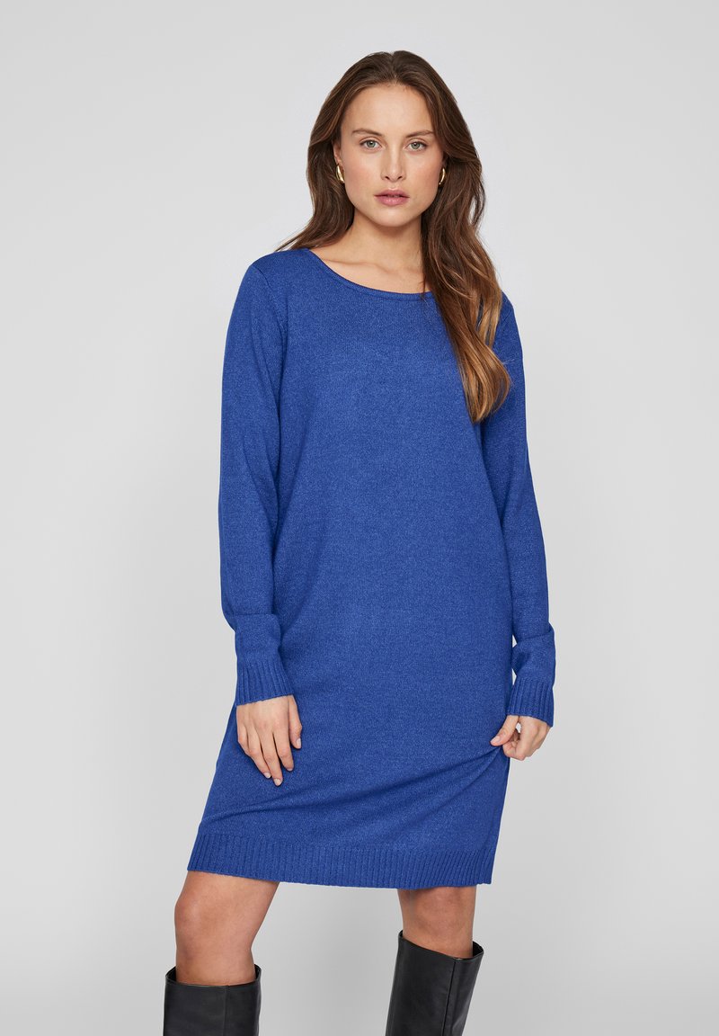 Långärmad, oversized klänning i ett djupblått stickat tyg. Har en bred halsringning och ribbade ärmslut, faller precis ovanför knäet.