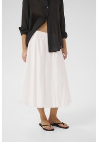 Jupe blanche, longueur genou, en tissu doux et léger avec une taille élastique. Associée à une chemise noire transparente à boutons et des tongs.