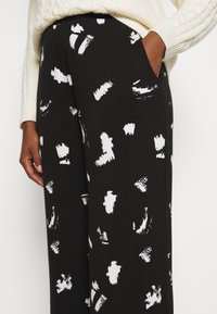 Pantalones de pierna ancha en tejido de algodón negro, con un patrón de pinceladas blancas, con bolsillos laterales y un corte relajado.