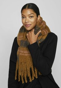 Brun franje-scarf lavet af blødt materiale, med et ternet mønster og nuancer af pink og blå, draperet om halsen.