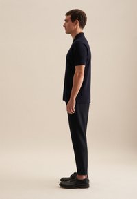 Granatowa koszulka polo z krótkim rękawem, zestawiona z dopasowanymi czarnymi spodniami i czarnymi butami. Proste, czyste linie i minimalne akcenty.