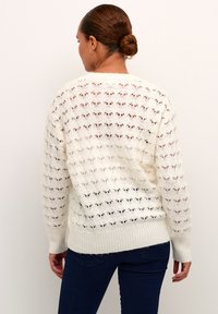 Cream knitted sweater with a lacy pattern and ribbed hem. Features long sleeves and a relaxed fit, showcasing an open weave texture.