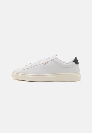 Baskets basses blanches avec semelle beige, fermeture à lacets, languette de talon noire et logo doré "BOSS" sur le côté sur fond uni.