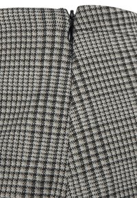 Gecontroleerde stof in zwart en grijs met een subtiel houndstooth patroon; heeft een zwarte rits aan de achterkant. Gestructureerd en textuurvol ontwerp.