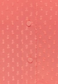 Tessuto rosa corallo con motivo a pois testurizzati e due bottoni rivestiti in tessuto cuciti lungo una cucitura verticale.