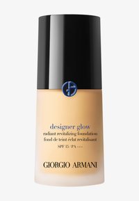 Glass foundation bottle with a rounded shape, gold liquid inside, matte black cap, and blue logo; text includes product name and SPF details.