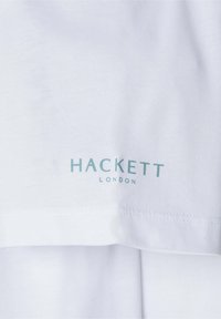 Bílá bavlněná tričko s logem "HACKETT LONDON" ve světle modré barvě na spodní části, s hladkou texturou a čistým stehem.