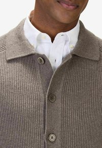 Brun ribbad tröja med krage, med fyra runda knappar och en vit skjorta under.