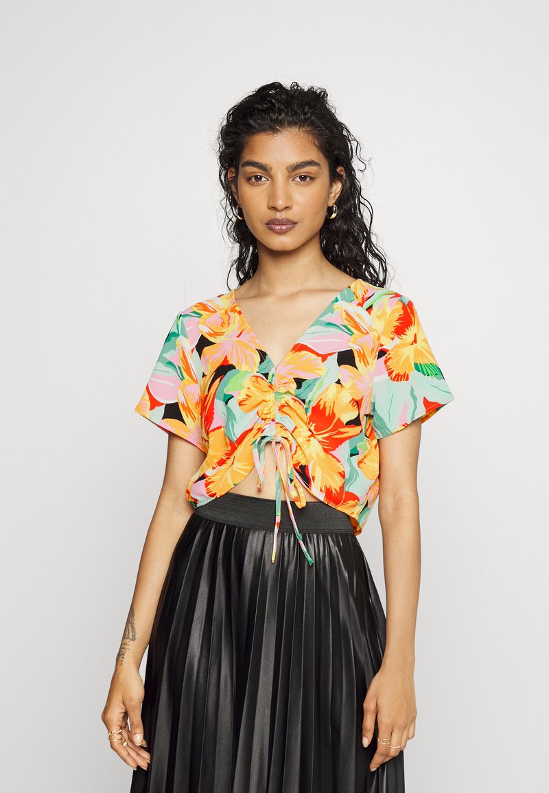 Top cropped floral com um padrão misto de laranja, rosa e verde sobre um fundo preto; apresenta um cordão na frente e mangas curtas.
