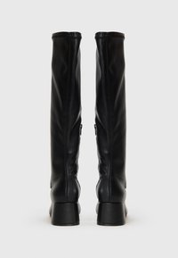 Bottes en cuir noir montantes avec une texture lisse, des talons ronds et des fermetures Éclair sur le côté. Elles présentent un design ajusté et des détails cousus.
