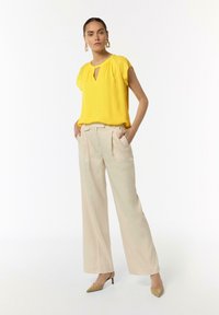 Żółta bluzka z krótkim rękawem i dekoltem w kształcie łezki, w połączeniu z beżowymi spodniami w szerokim kroju i cielistymi szpilkami. Prosty design, lekka tkanina.